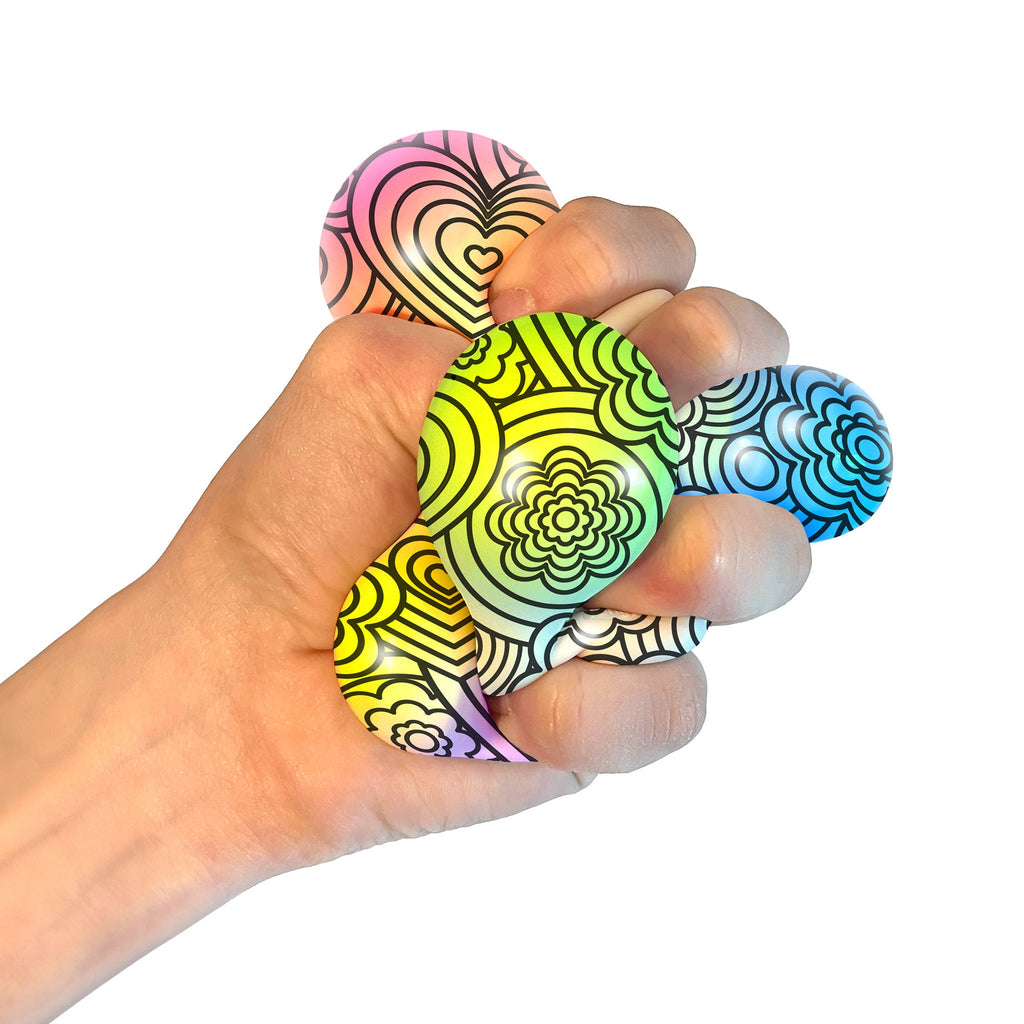 A hand squeezing a NeeDoh Press-Doh C7. The colorful doh is visible through the white and black designs of the exterior.